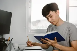 Young man reading book and writing notes.